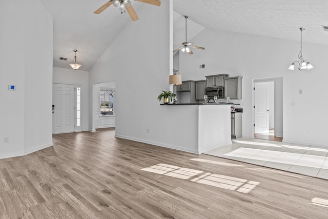 unfurnished living room with ceiling fan with notable chandelier, light wood-type flooring, visible vents, and baseboards