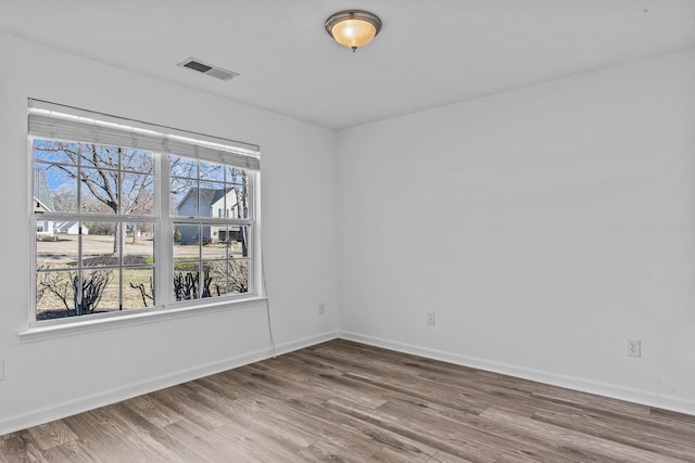 empty room featuring wood finished floors, visible vents, and baseboards