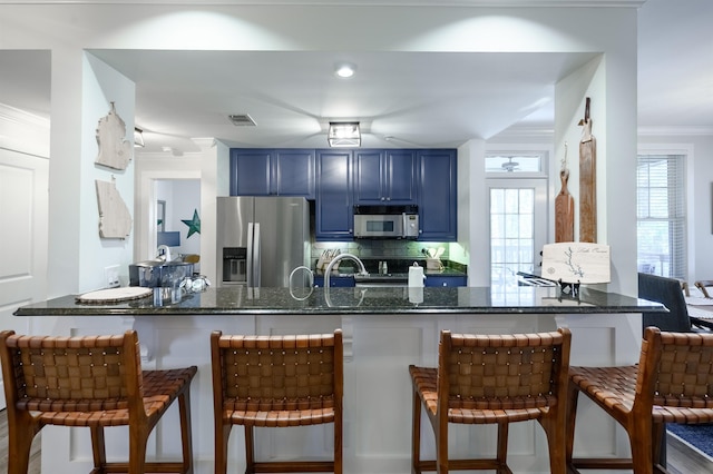 kitchen featuring blue cabinets, appliances with stainless steel finishes, dark stone countertops, and a kitchen bar