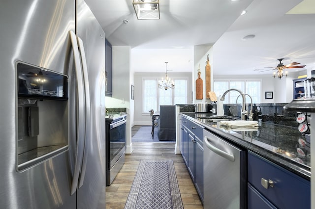 kitchen featuring appliances with stainless steel finishes, decorative light fixtures, sink, dark stone countertops, and light wood-type flooring