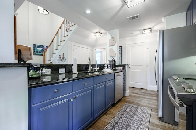 kitchen with blue cabinetry, sink, dark stone countertops, appliances with stainless steel finishes, and light hardwood / wood-style floors