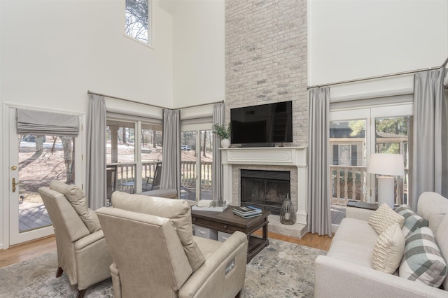 living area with plenty of natural light, a brick fireplace, a towering ceiling, and wood finished floors