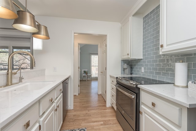 kitchen with light wood finished floors, backsplash, white cabinets, stainless steel appliances, and a sink