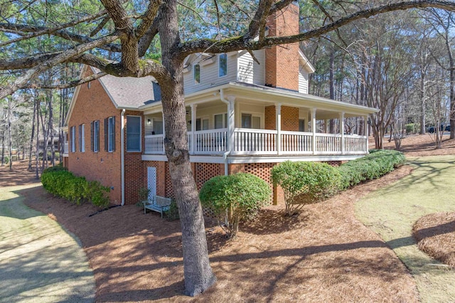 farmhouse inspired home featuring brick siding, a porch, and a chimney