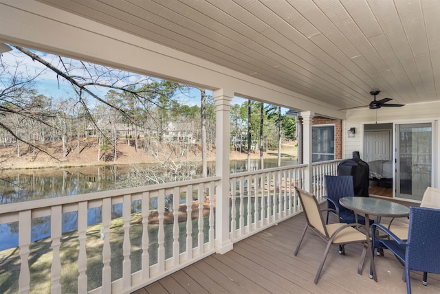 wooden deck with outdoor dining area, a ceiling fan, and a water view