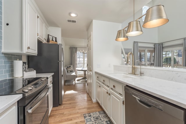 kitchen featuring visible vents, a sink, white cabinets, light wood-style floors, and appliances with stainless steel finishes