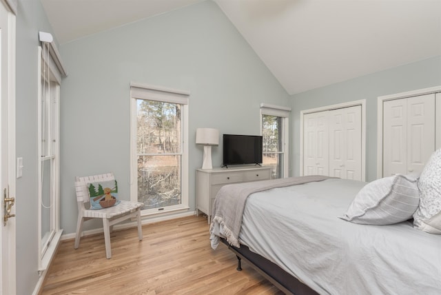 bedroom with light wood-style flooring, baseboards, multiple closets, and high vaulted ceiling