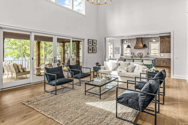 living room with light wood-style floors, french doors, a high ceiling, and a notable chandelier