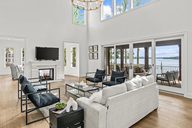 living area featuring a high ceiling, a notable chandelier, plenty of natural light, and a glass covered fireplace
