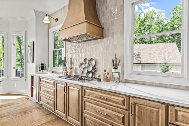 interior space featuring premium range hood, stainless steel gas stovetop, light stone counters, light wood-type flooring, and decorative backsplash