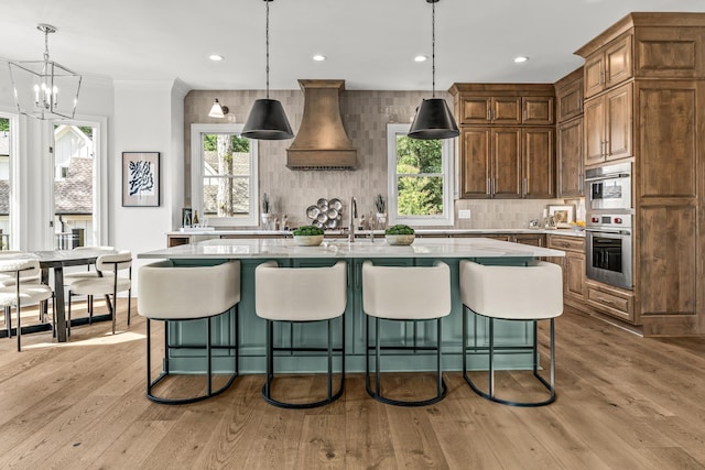 kitchen with a center island with sink, tasteful backsplash, custom range hood, and light wood-type flooring
