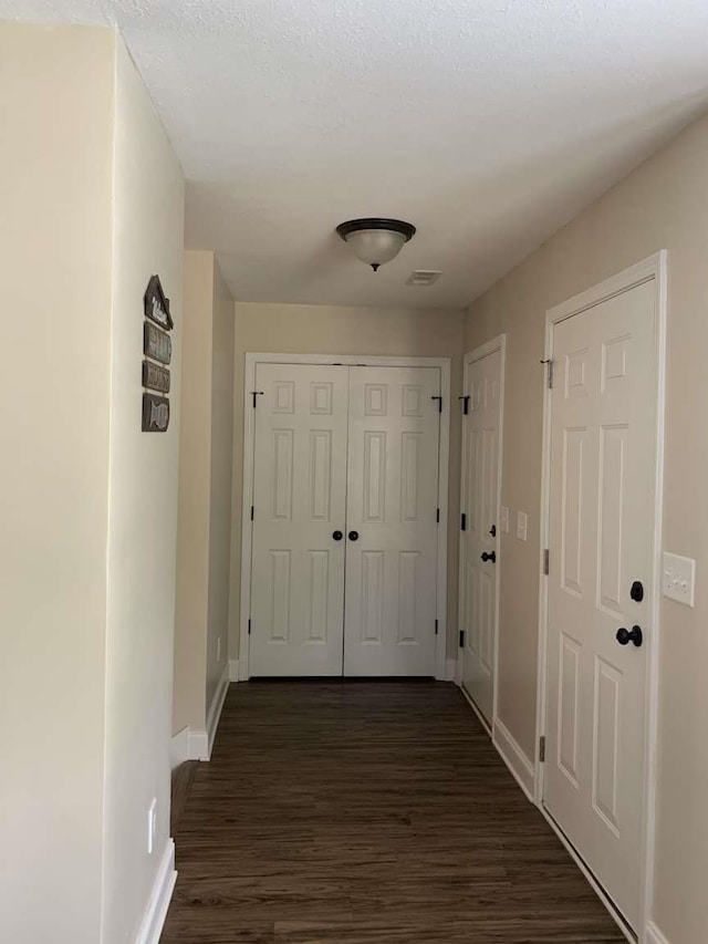 hall featuring dark wood-type flooring, visible vents, and baseboards