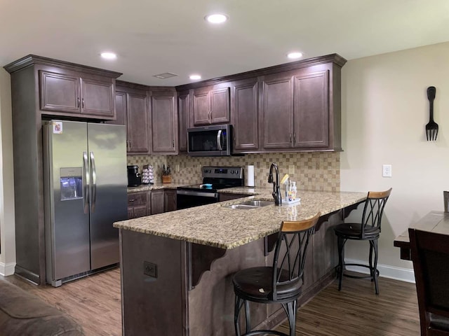 kitchen featuring light wood finished floors, a peninsula, a sink, appliances with stainless steel finishes, and tasteful backsplash