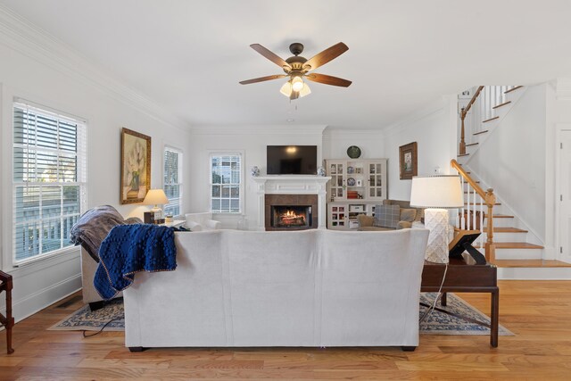 living room featuring hardwood / wood-style flooring, a tiled fireplace, ceiling fan, and crown molding