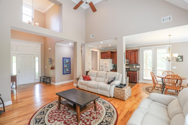 living room featuring a high ceiling, crown molding, ceiling fan with notable chandelier, and light wood-type flooring