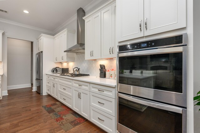 kitchen with white cabinetry, ornamental molding, wall chimney exhaust hood, and stainless steel appliances