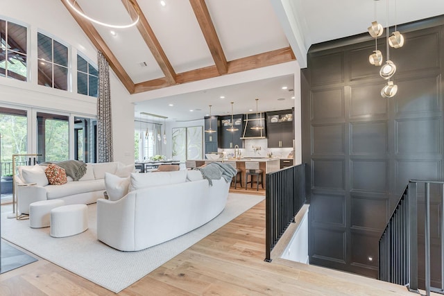 living room with sink, light hardwood / wood-style flooring, beamed ceiling, and a high ceiling