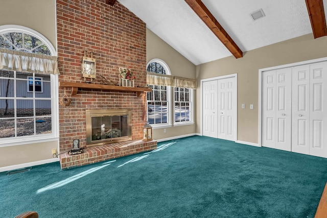 unfurnished living room with beamed ceiling, a healthy amount of sunlight, a brick fireplace, and carpet flooring