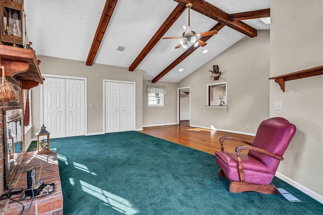 living area with a brick fireplace, ceiling fan, beamed ceiling, and carpet