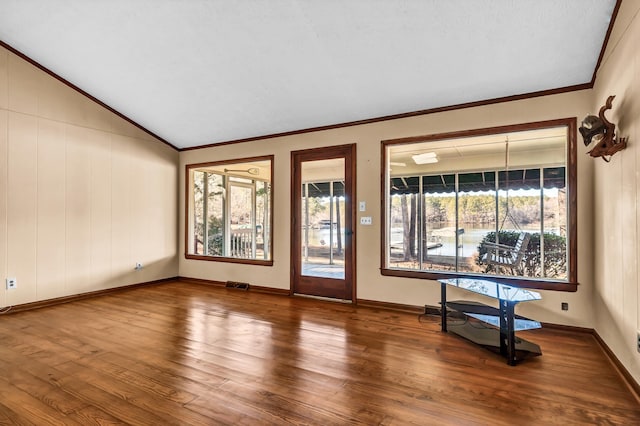 empty room with hardwood / wood-style flooring, ornamental molding, plenty of natural light, and vaulted ceiling