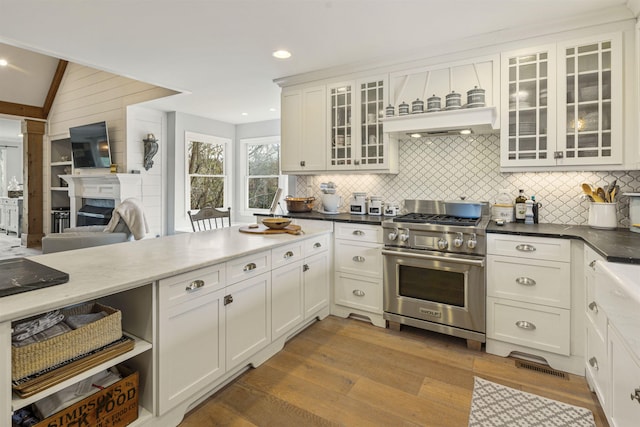 4410 Lower Apalachee Rd, Madison, GA 30650 - kitchen with backsplash, dark wood-style floors, stainless steel stove, white cabinets, and a glass covered fireplace