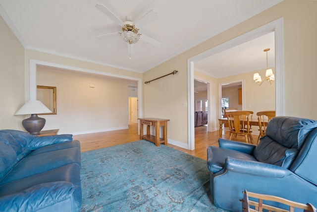 living area featuring baseboards, wood finished floors, crown molding, and ceiling fan with notable chandelier