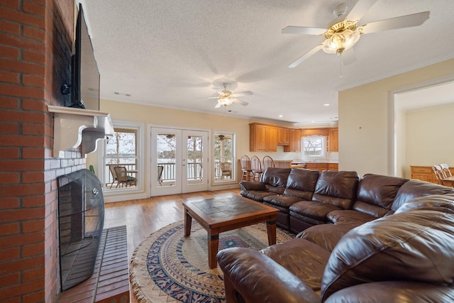 living room featuring wood finished floors, a fireplace, french doors, a textured ceiling, and crown molding