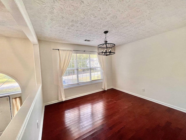 unfurnished dining area with dark hardwood / wood-style flooring, a textured ceiling, and an inviting chandelier