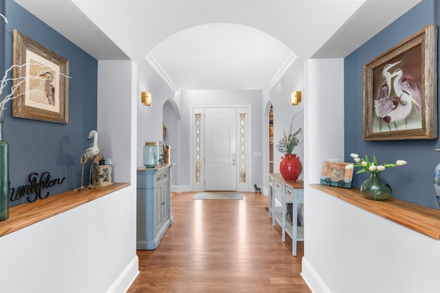 foyer with wood finished floors, arched walkways, and baseboards