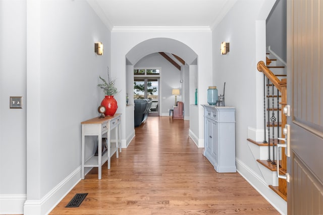 hallway featuring crown molding, light wood-style floors, arched walkways, and baseboards