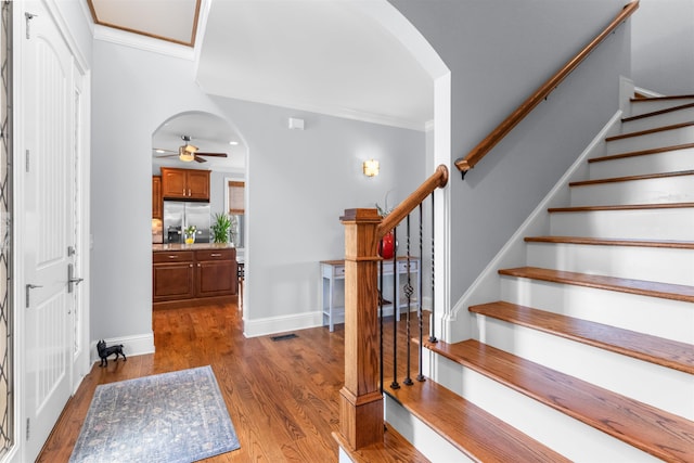 entrance foyer with stairway, wood finished floors, a ceiling fan, arched walkways, and crown molding