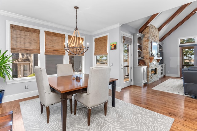 dining space featuring lofted ceiling with beams, wood finished floors, a stone fireplace, baseboards, and a chandelier