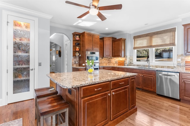 kitchen featuring ornamental molding, a sink, stainless steel appliances, arched walkways, and ceiling fan