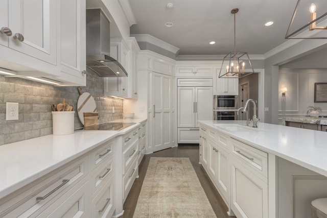 kitchen with white cabinetry, sink, hanging light fixtures, crown molding, and wall chimney range hood