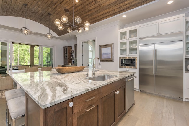 kitchen with decorative light fixtures, lofted ceiling, sink, white cabinets, and built in appliances