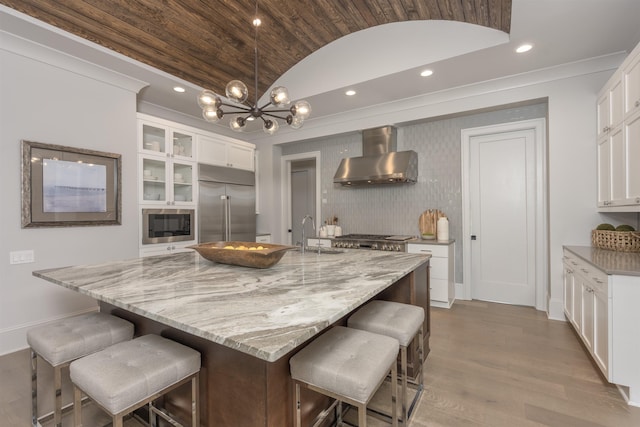 kitchen with a large island, wall chimney range hood, and white cabinetry