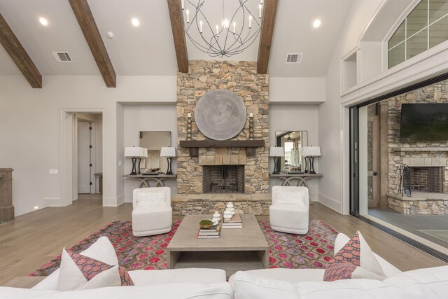 living room with beamed ceiling, a stone fireplace, an inviting chandelier, and light wood-type flooring