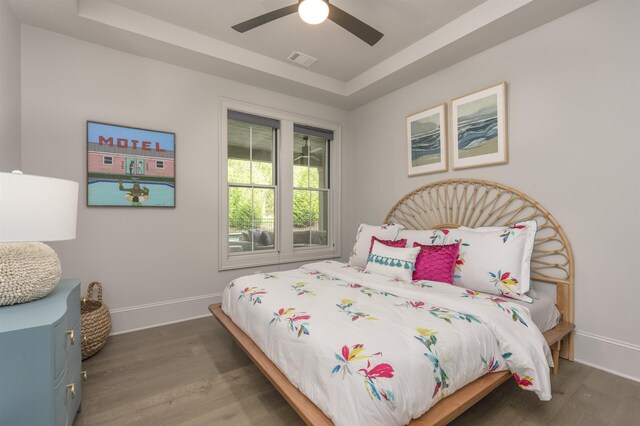 bedroom featuring a raised ceiling, dark hardwood / wood-style floors, and ceiling fan