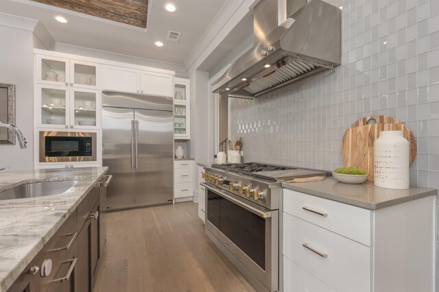 kitchen featuring sink, extractor fan, light stone counters, built in appliances, and white cabinets