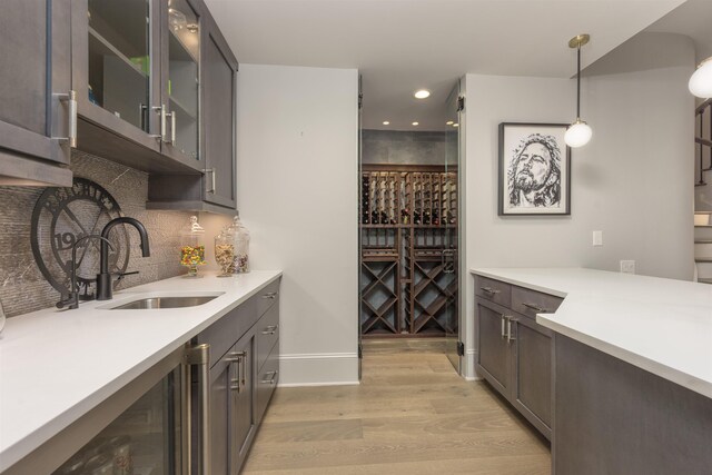 bar with sink, decorative backsplash, decorative light fixtures, beverage cooler, and light wood-type flooring