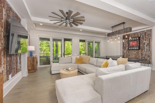 living room with ceiling fan, wood-type flooring, and a raised ceiling