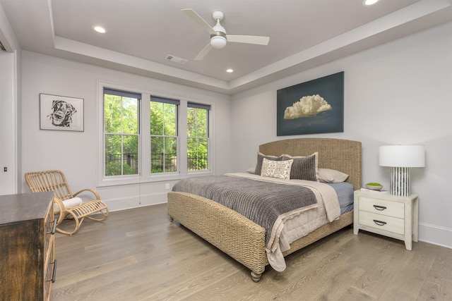 bedroom with hardwood / wood-style floors, a raised ceiling, and ceiling fan