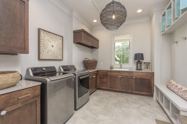 clothes washing area with washer and dryer, crown molding, sink, and cabinets