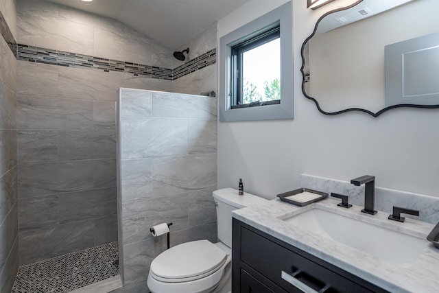 bathroom featuring vanity, lofted ceiling, tiled shower, and toilet