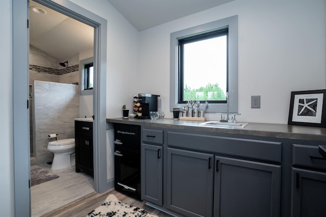 bathroom featuring hardwood / wood-style floors, vanity, a tile shower, vaulted ceiling, and toilet