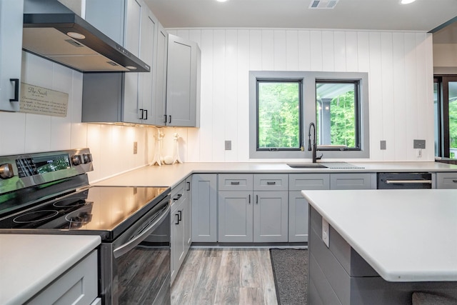 kitchen with sink, gray cabinetry, stainless steel appliances, wall chimney range hood, and light hardwood / wood-style flooring