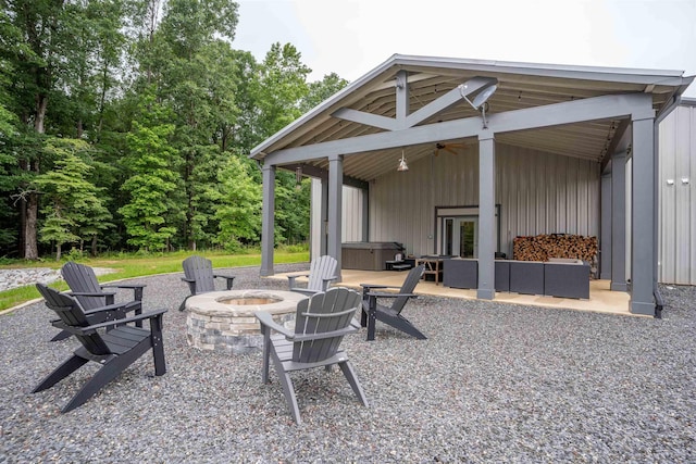 view of patio with ceiling fan, a hot tub, and an outdoor living space with a fire pit