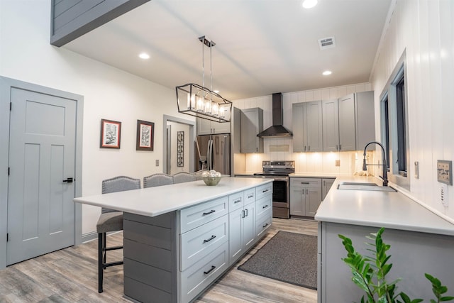 kitchen featuring appliances with stainless steel finishes, decorative light fixtures, sink, a breakfast bar area, and wall chimney range hood