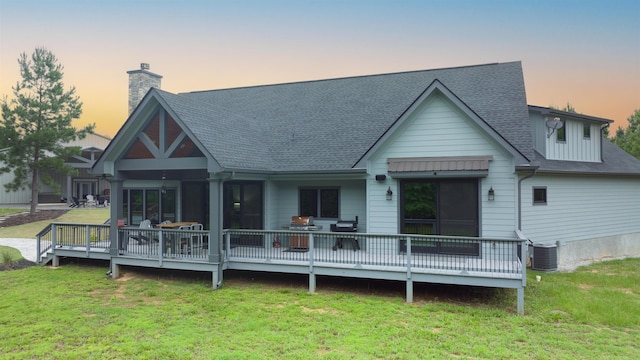 back house at dusk featuring central AC unit, a yard, and a deck