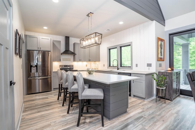 kitchen featuring wall chimney exhaust hood, sink, appliances with stainless steel finishes, gray cabinets, and pendant lighting